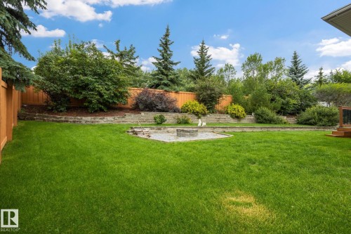 Expansive lawn area, wood privacy fencing, stone-lined tiered landscaping, integrated fire pit, and mature trees - 15 Orchid Place, St. Albert, AB - Outdoor