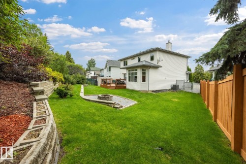 Expansive backyard featuring a manicured lawn, concrete block retaining walls, a wood privacy fence, and a built-in fire pit area with gravel - 15 Orchid Place, St. Albert, AB - Outdoor With Backyard
