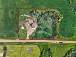 Aerial view of a rectangular property featuring a central residence with a brown roof, undeveloped land, surrounding green fields, and a road bordering the property - 