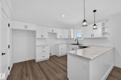 Living Space # 1 Modern kitchen featuring wood-finish flooring, white cabinetry with black hardware, white subway tile backsplash, white countertops, and pendant lighting - 