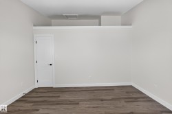 Living Space # 1 Room featuring wood-finish flooring, crisp white baseboards, a white panel door with black hardware, and light neutral wall paint - 