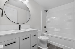 Living Space # 1 Modern bathroom featuring a single vanity with integrated sink, matte black fixtures, an oval mirror, and a white bathtub with shower surround - 