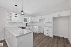 Living Space # 2 Modern kitchen featuring white cabinetry, subway tile backsplash, light-toned stone-finish countertops, wood-finish flooring, and matte black fixtures - 