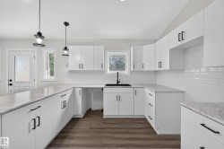 Living Space # 2  Modern kitchen featuring white shaker-style cabinetry, light-toned countertops, a white subway tile backsplash, matte black hardware, and wood-finish flooring - 