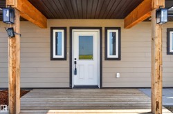 Inviting front entryway featuring a white panel door with sidelight windows, tan horizontal siding, and dark trim - 