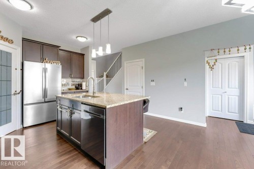 Kitchen featuring a central island with a granite-style countertop, integrated sink, and dishwasher - 2436 18 Avenue Nw, Edmonton, AB 