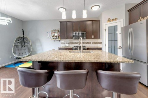 Kitchen featuring a central island with granite countertops, wood-finish cabinetry, stainless steel appliances, and a tiled backsplash - 2436 18 Avenue Nw, Edmonton, AB 