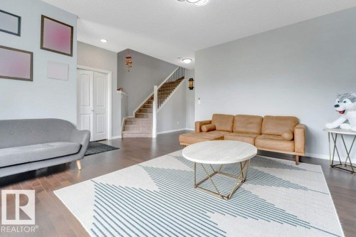 Spacious open-concept living area featuring wood-finish flooring, light-toned walls, a staircase with carpeted treads and white risers, and a double-door closet - 2436 18 Avenue Nw, Edmonton, AB 