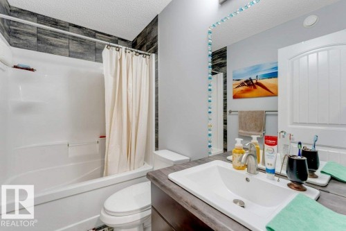 White drop-in bathtub with tiled surround, vanity with an integrated sink, and a large wall mirror - 2436 18 Avenue Nw, Edmonton, AB 
