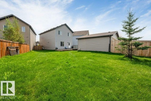 Expansive grassy yard with a wooden fence, featuring a detached garage with siding, and a rear deck - 2436 18 Avenue Nw, Edmonton, AB 