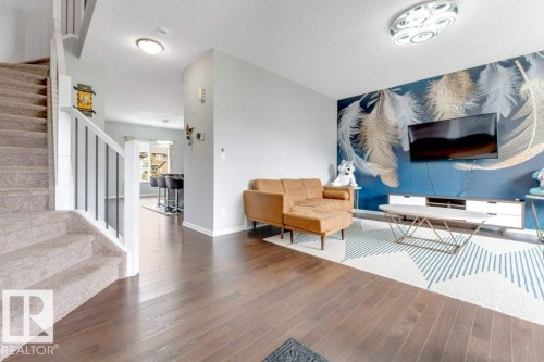 Wood-finish flooring, staircase with carpeted treads and white risers, contemporary ceiling light fixture, accent wall with feather motif, built-in media console - 2436 18 Avenue Nw, Edmonton, AB 