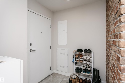 Entryway featuring a white door with brushed nickel hardware, light gray walls, exposed brick accent wall, and tiled flooring - #208 9907 91 Av Nw, Edmonton, AB - Indoor Photo Showing Other Room