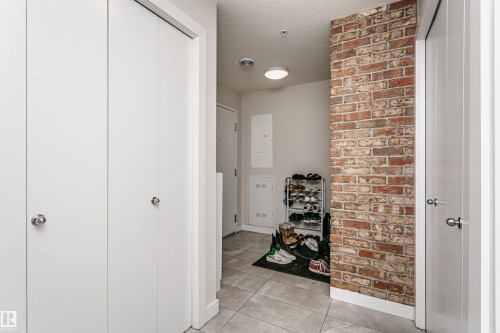 Foyer featuring a brick accent wall, light-toned floor tile, and multiple white panel doors - #208 9907 91 Av Nw, Edmonton, AB - Indoor Photo Showing Other Room