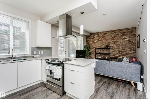 Modern open-concept living space featuring a kitchen with white cabinetry, stainless steel appliances, and a quartz countertop island - #208 9907 91 Av Nw, Edmonton, AB - Indoor Photo Showing Kitchen