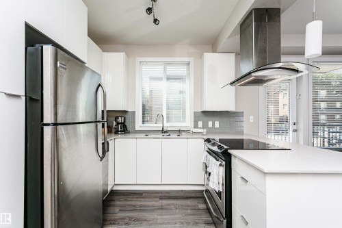 Modern kitchen featuring stainless steel appliances, white cabinetry, light countertops, subway tile backsplash, and wood-finish flooring - #208 9907 91 Av Nw, Edmonton, AB - Indoor Photo Showing Kitchen With Stainless Steel Kitchen With Upgraded Kitchen