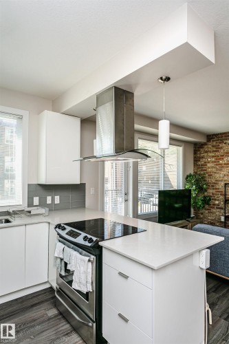 Modern kitchen featuring white cabinetry, a light-colored countertop, stainless steel appliances, a tile backsplash, and wood-finish flooring - #208 9907 91 Av Nw, Edmonton, AB - Indoor Photo Showing Kitchen With Upgraded Kitchen