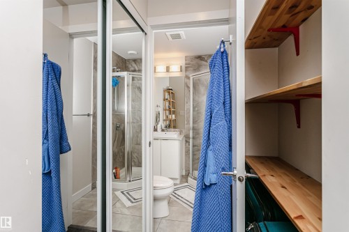 Bathroom featuring a glass-enclosed shower, white vanity with integrated sink, modern wall-mounted lighting, and gray floor tiling - #208 9907 91 Av Nw, Edmonton, AB - Indoor
