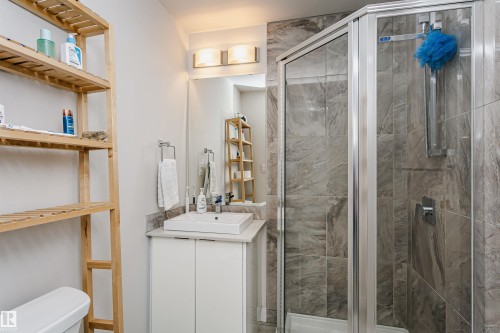 Bathroom featuring a corner glass-enclosed shower with gray tiled walls, a white vanity cabinet, a rectangular vessel sink, and a wall-mounted mirror - #208 9907 91 Av Nw, Edmonton, AB - Indoor Photo Showing Bathroom