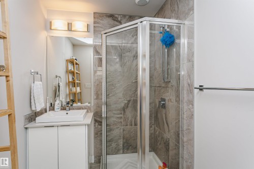 Bathroom featuring a glass-enclosed shower with tile surround, a rectangular vessel sink, a vanity with white cabinetry, and a wall-mounted light fixture - #208 9907 91 Av Nw, Edmonton, AB - Indoor Photo Showing Bathroom