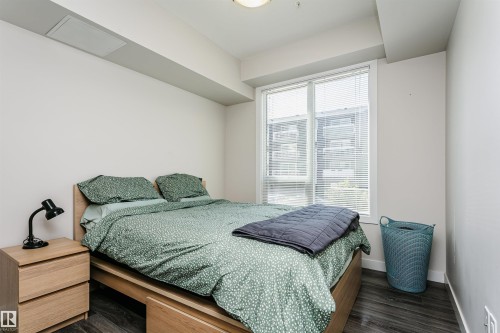 Bedroom featuring a large window with blinds, wood-finish flooring, and light-colored walls - #208 9907 91 Av Nw, Edmonton, AB - Indoor Photo Showing Bedroom