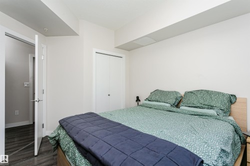 Bedroom featuring light-toned walls, wood-finish flooring, a built-in closet with bi-fold doors, a modern light fixture, and an open doorway - #208 9907 91 Av Nw, Edmonton, AB - Indoor Photo Showing Bedroom