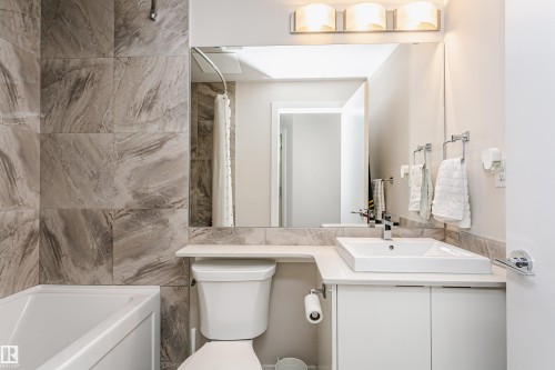 Bathroom featuring a white rectangular vessel sink, coordinating countertop, vanity with white cabinetry, large vanity mirror, and three-light fixture - #208 9907 91 Av Nw, Edmonton, AB - Indoor Photo Showing Bathroom