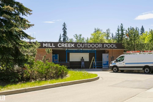 Mill Creek Outdoor Pool building featuring brick and dark paneling, prominent signage, and a paved approach - #208 9907 91 Av Nw, Edmonton, AB - Outdoor