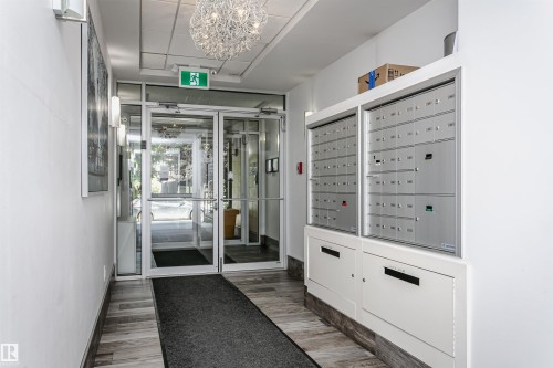 Building entryway featuring a glass door system, wood-finish flooring, and built-in mailboxes with parcel lockers - #208 9907 91 Av Nw, Edmonton, AB - Indoor Photo Showing Other Room