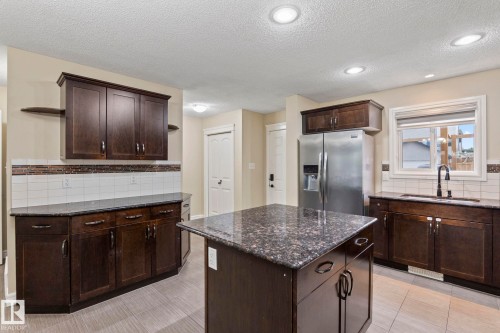 Kitchen featuring dark wood cabinetry, a central island with a stone countertop, tile backsplash, and recessed lighting - 1209 30 Avenue Nw, Edmonton, AB - Indoor Photo Showing Kitchen