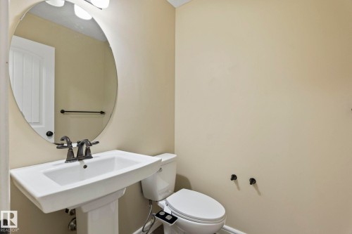 Pedestal sink with a dark bronze faucet, oval mirror, and wall-mounted light fixture - 1209 30 Avenue Nw, Edmonton, AB - Indoor Photo Showing Bathroom