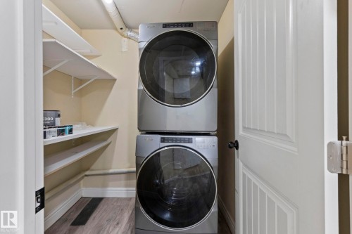 Stacked laundry appliances with wood-finish flooring, white shelving, and a paneled door - 1209 30 Avenue Nw, Edmonton, AB - Indoor Photo Showing Laundry Room
