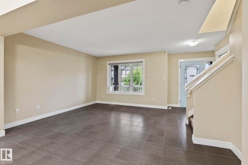 Spacious room featuring tile flooring, painted walls, a large window, and a staircase with white railing - 1209 30 Avenue Nw, Edmonton, AB - Indoor Photo Showing Other Room