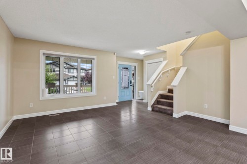 Expansive ceramic tile flooring, bright window with white trim, light blue entry door, and carpeted staircase with white handrails - 1209 30 Avenue Nw, Edmonton, AB - Indoor