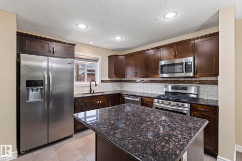 Kitchen featuring dark wood-finish cabinetry, stainless steel appliances, speckled stone countertops, a central island, and recessed lighting - 1209 30 Avenue Nw, Edmonton, AB - Indoor Photo Showing Kitchen