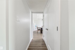 Hallway featuring wood-finish flooring, white walls, and white doors with contemporary hardware - 