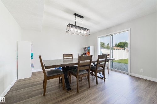 Wood-finish flooring, white walls, and a contemporary linear chandelier with a metal frame - 4614 53 Ave, Calmar, AB - Indoor Photo Showing Dining Room