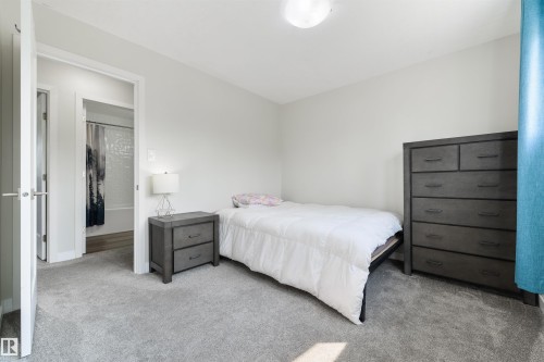 Light gray wall paint, gray carpet flooring, ceiling-mounted light fixture, white interior door with brushed nickel hardware, and an adjacent bathroom with a white bathtub - 4614 53 Ave, Calmar, AB - Indoor Photo Showing Bedroom