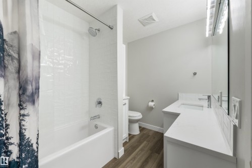White subway tile shower surround with chrome fixtures, white bathtub, vanity with integrated sink, white countertop, wood-finish flooring - 4614 53 Ave, Calmar, AB - Indoor Photo Showing Bathroom