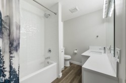 White subway tile shower surround with chrome fixtures, white bathtub, vanity with integrated sink, white countertop, wood-finish flooring - 