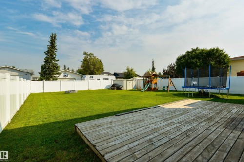 Expansive backyard featuring a wood deck, manicured lawn, and white privacy fencing - 4614 53 Ave, Calmar, AB - Outdoor With Backyard