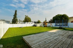 Expansive backyard featuring a wood deck, manicured lawn, and white privacy fencing - 