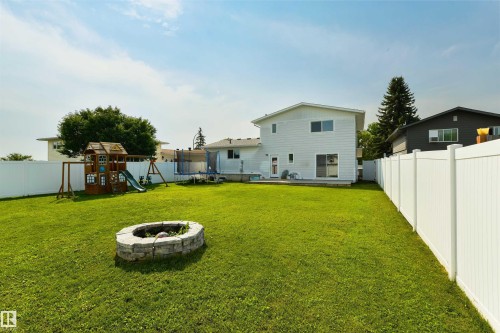 Expansive green lawn featuring a built-in stone fire pit, a white privacy fence, and a rear exterior with a sliding glass door - 4614 53 Ave, Calmar, AB - Outdoor With Backyard
