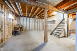 Unfinished basement with exposed wood framing, concrete flooring, and an interior staircase - 