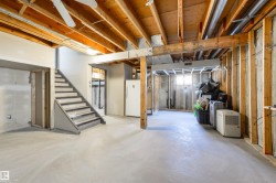 Unfinished basement with exposed wood joists and framing, a staircase with painted risers, and concrete flooring - 