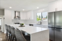 Expansive kitchen island with a light-toned countertop, white cabinetry, stainless steel appliances, patterned tile backsplash, and recessed lighting - 