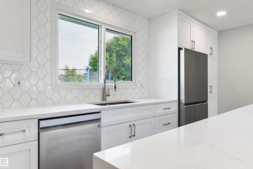 White shaker-style cabinetry, quartz countertops, hexagonal tile backsplash, stainless steel appliances, and an undermount sink with a gooseneck faucet - 4614 53 Ave, Calmar, AB - Indoor Photo Showing Kitchen