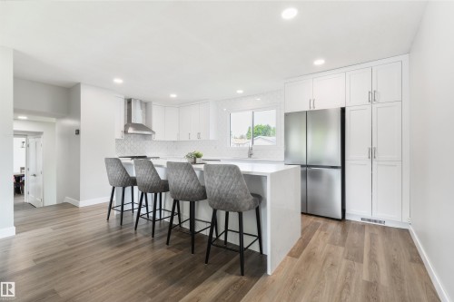 Modern kitchen featuring an island with seating, stainless steel appliances, extensive white cabinetry, and wood-finish flooring - 4614 53 Ave, Calmar, AB - Indoor Photo Showing Kitchen With Upgraded Kitchen