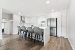 Modern kitchen featuring an island with seating, stainless steel appliances, extensive white cabinetry, and wood-finish flooring - 