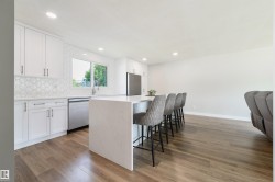 White shaker cabinetry, patterned tile backsplash, stainless steel appliances, waterfall-edge island, and wood-finish flooring - 