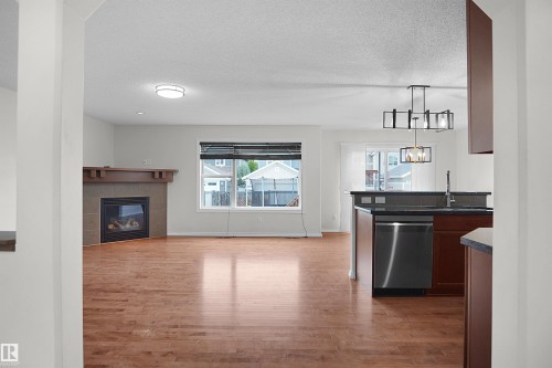 Hardwood-finish flooring, built-in fireplace with stone surround and wood mantel, stainless steel dishwasher, and contemporary chandelier - 8432 18 Avenue Sw, Edmonton, AB - Indoor With Fireplace